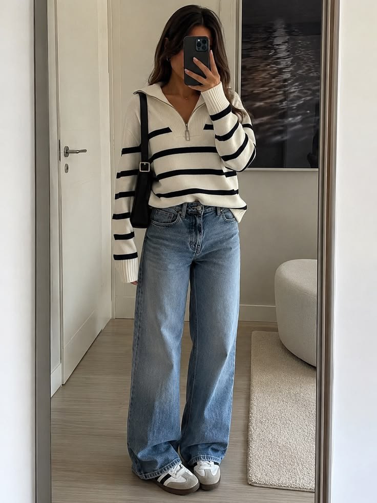 A phone mirror selfie: striped half-zip knit, shoulder bag, wide light jeans and trainers.