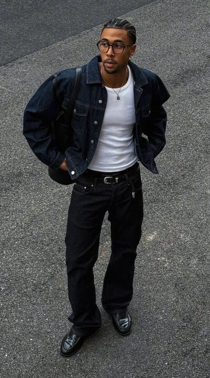 A man in a dark denim jacket, white tank and black jeans.